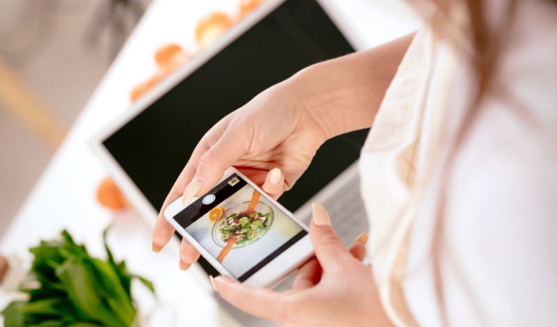 Woman holding a cell phone over a camera with a food photo on it